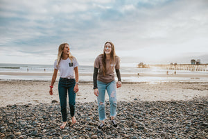 Two women laughing together while wearing nöz sunscreen on their nose, walking away from the ocean. 